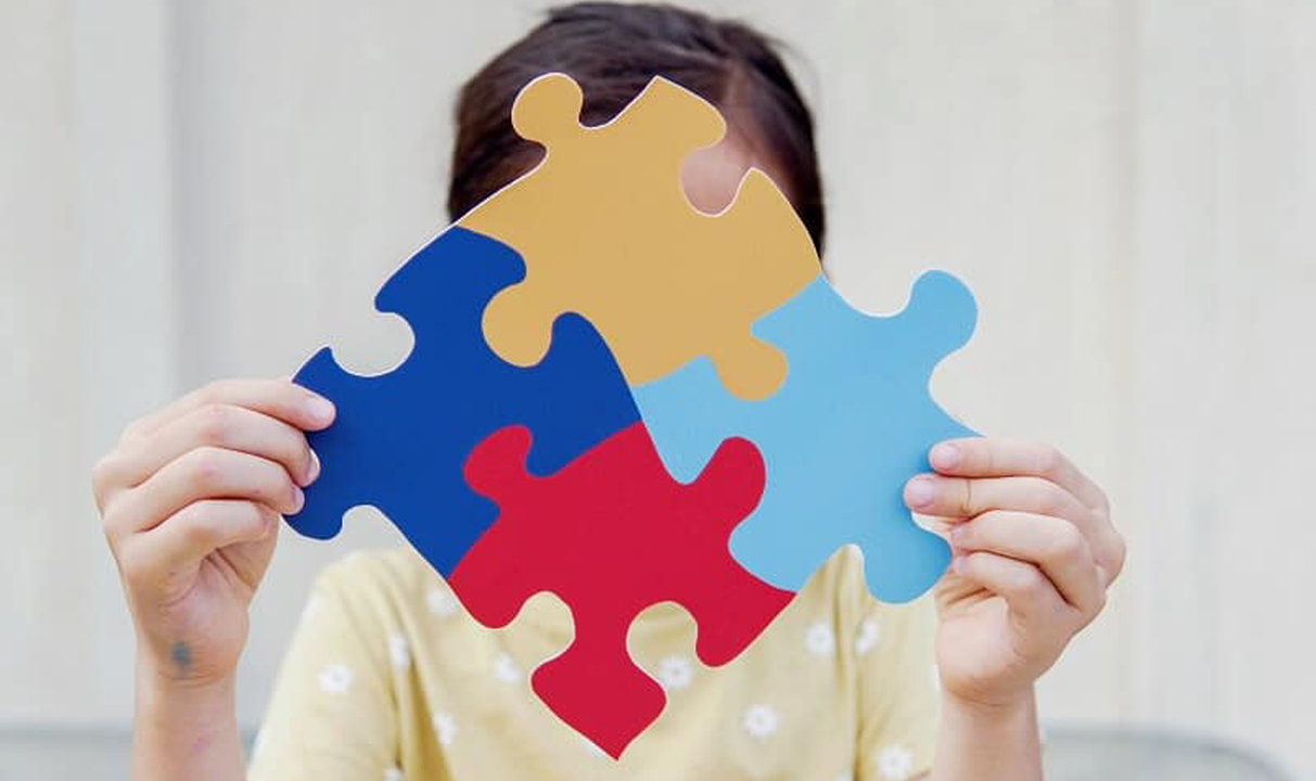 Una niña sujeta un puzzle con el símbolo del autismo