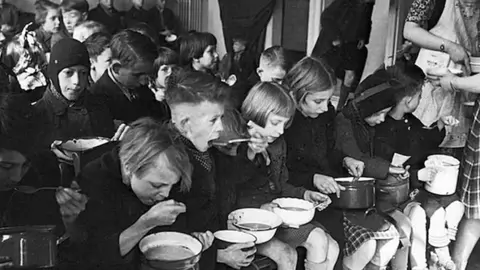 [Dar clic y arrastrar para mover]
Ni&ntilde;os comen alimentos donados por una organizaci&oacute;n eclesi&aacute;stica durante la gran hambruna que sufri&oacute; Pa&iacute;ses Bajos entre 1944 y 1945. Menno Huizinga / Wikimedia Commons