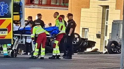 Una ambulacia del 112 recoge a uno de los heridos, tras volcar el veh&iacute;culo sustraido